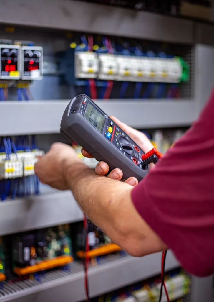 Betriebstechniker prüft mit einem Messgerät etwas am Schaltschrank